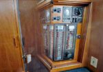Wooden cabinet houses an old electrical panel with multiple breakers, gauges, and switches.