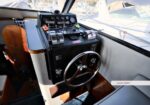 Lower-helm steering console of a motorboat with a wooden wheel, gauges, and controls at the helm, overlooking a marina