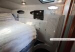 Owner's cabin aboard a yacht: a plush bed with white fur blanket on the left, built-in storage cabinets, a wall-mounted TV, portholes, and a small skylight above, a cozy compact living space.