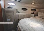 Compact boat cabin with a bed on the right and built-in cabinets along the port wall, small porthole windows ahead.