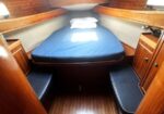 Cozy boat cabin with a blue-mattressed bed on a V-shaped frame, surrounded by wooden shelves and benches.