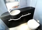 Compact airplane lavatory with a white sink bowl in a black vanity, a toilet to the right, and a small window above.