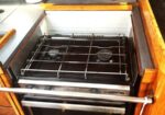 Gas stovetop with two burners and an open oven below, installed in wooden kitchen cabinetry.