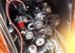 Close-up of a small marine engine in a wooden engine compartment, with belts, hoses, and a red oil filter visible