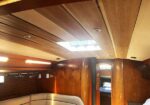 Wood-paneled yacht cabin with a curved cream sofa, small table, and a skylight in the ceiling.