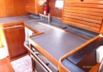 Wood-paneled boat galley with a metallic countertop, stove oven, and built-in cupboards; a red fire extinguisher mounted on the wall nearby.