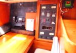 Wood-paneled boat cabin with a tall electrical distribution panel, switches and gauges, plus a radio and a binder on the counter.