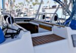 Open cockpit of a sailboat at a marina, featuring a wood-planked deck, ropes, and seating areas.