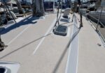 Wide view of a sailboat deck at a marina, showing a raised hatch, winches, and lines with other moored boats in the background.