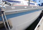 Close-up of a sailboat hull moored at a marina, featuring a blue stripe, coiled ropes, and a fender along the dock.