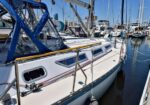 White sailboat moored at a marina with blue canvas cover and stainless rails along the deck at a sunny harbor.