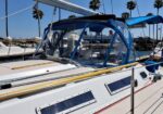 White sailboat moored at a sunny marina with a blue cockpit dodger and palm trees in the background