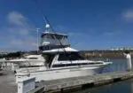 White sport fishing boat docked at a wooden marina, with clear blue sky and calm water in the background.