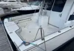 White motorboat stern with built-in seating and central pedestal, docked at a marina.
