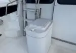 White cylindrical marine water tank with a lid and small spout on a boat deck, beside a metal ladder and cabin door.