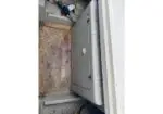 Open metal electrical cabinet in a dirty utility space, showing a perforated floor grate and exposed wiring.