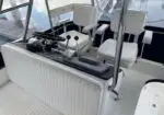 Helm console on a white boat with steering wheel, throttle levers, and white cushioned seats behind the console