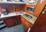 Compact boat galley with wooden cabinetry, microwave, sink, two-burner stove, and coffee maker on the counter.
