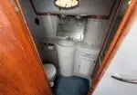 Compact boat head with a white pedestal sink, mirrored cabinet above, small toilet on the left, a louvered cabinet on the right, blue carpet, and wood trim around the doorway.