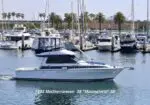 White motor yacht cruising in a marina with other boats and palm trees in the background; hull text reads 1993 Mediterranean 38 'Moonshine' 38'.