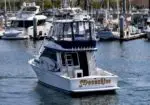 White motor yacht named Moonshine cruising in a marina with other boats in the background.