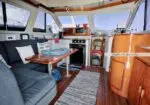 Cozy boat salon with navy Sofas, wooden table, and marine decor; large port windows show blue sky outside.