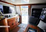 Interior of a boat saloon with wooden cabinets, a blue sofa, and a table, door open to a marina outside.