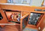 Wood-paneled boat cabin with an open liquor cabinet showing bottles beside a starboard electrical control panel and switches