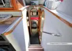 Wood-trimmed companionway stairs leading to a cabin aboard a boat or yacht, with mirrored doors and a bed visible at the far end.