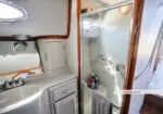 Compact yacht bathroom with a glass shower enclosure, sink with faucet, round porthole window, and wooden trim.