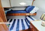 Two-berth guest cabin on a boat with an upper bunk and a lower bunk, both with blue striped bedding and wooden cabinetry.