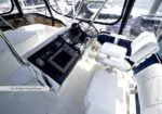 Flybridge helm station on a motor yacht, with steering wheel, navigation screens, radios, and white captain's chair.