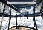Inside a boat cabin with metal framing and large windows; a caption reads: 'Moonshine has the much sought after hardtop with plenty of headroom. Her isenglass is in like new condition!'.