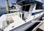 White motor yacht with a spacious cockpit at a marina, showing a captain's door, seating area, and railing along the deck.
