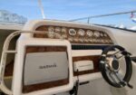 Boat helm with a wood dashboard, many round gauges, a Garmin navigation display, and a black steering wheel in a yacht cockpit.