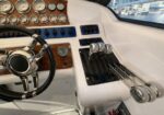 Boat helm with polished steering wheel and throttle levers on a white dashboard, wood trim, and gauges visible.