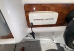 White Standard Horizon marine VHF radio mounted on a wood panel in a boat, with a cord hanging down.