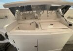 White boat galley with a dual basin sink, chrome faucet, and a covered stovetop—the lid is raised to reveal the cooking area; cabinets below for storage.