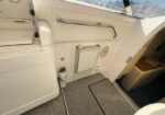 Boat deck entry with white padded wall, a rectangular hatch/door, and a small fire extinguisher on the floor nearby.