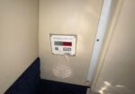 Environmental control unit panel with digital display and four buttons mounted on a beige wall above a circular vent.