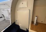 Interior of a small aircraft galley with a beige cabinet, closed hatch, and towel roll on a wooden counter beside an open door to the exterior cabin.