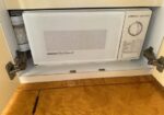 Under-cabinet white microwave oven in a kitchen cabinet, with a round control dial on the right and vent in the center.