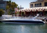 White and navy motor yacht docked at a marina with a red-and-white striped awning in the background.