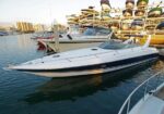 White speedboat docked at a marina with stacked boats on racks in the background, calm water reflecting the scene.