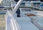 White luxury motorboat deck with cushioned seating and a wooden folding table, control console visible in background at a marina.