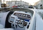 Close-up of a luxury motorboat cockpit with a multi-gauge dashboard, steering wheel, and GPS, docked at a marina.
