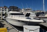 Two white motor yachts moored at a marina under a clear blue sky, with water, pilings, and buildings in the background.