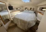 Boat cabin with a center queen bed, built‑in drawers and cabinets, mirrored wall panels, small TV, and porthole windows; skylight above.