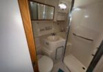 Compact boat bathroom with sink, mirror cabinet, toilet, and enclosed glass-door shower with a grab bar.