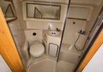 Compact boat/RV bathroom with a toilet, sink, mirrored cabinet, and separate shower stall; soap on the sink.